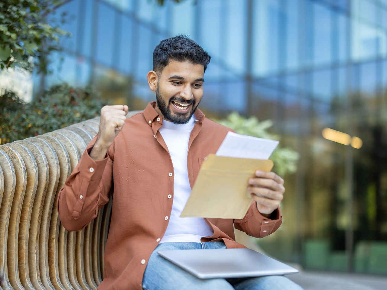 A smiling aspirant on a campus bench, celebrating while reading a result letter